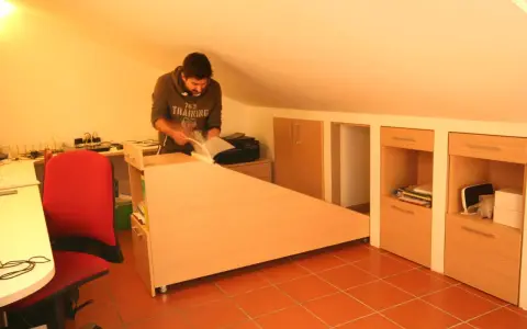 Uomo in mansarda con idee sottotetto molto basso: scrivania angolare, armadi a muro e sedia rossa.