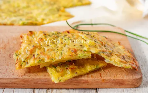 Schiacciata di zucchine dorata e croccante, con erbe aromatiche, servita su un tagliere di legno.