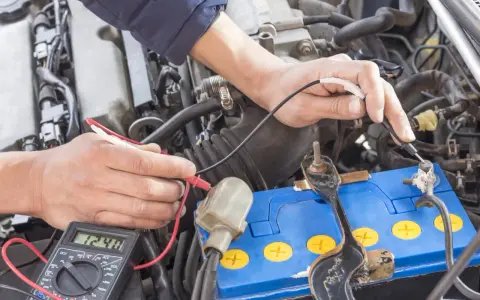 Mechanik sprawdza napięcie akumulatora za pomocą multimetru. Wynik 12.48V wskazuje na jego stan.