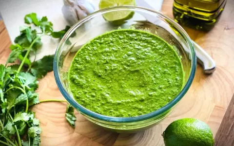 Frisch zubereitetes mojo verde in einer Glasschüssel, umgeben von Koriander, Knoblauch, Limetten und Olivenöl.
