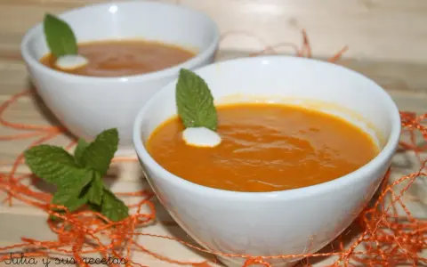 Dos cuencos blancos con crema de calabaza naranja, decorados con menta y un toque de nata.