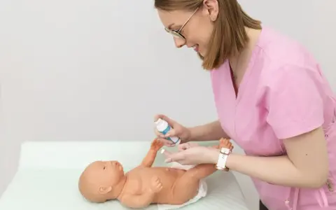 Uczymy się, co ile zmieniać pieluszkę noworodkowi. Pielęgniarka pokazuje na lalce, jak dbać o higienę maluszka.