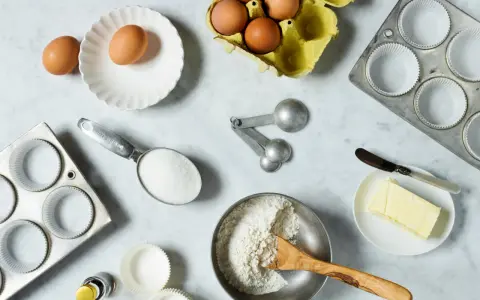 Backzutaten: Eier, Mehl, Zucker, Butter, Muffinförmchen und Messlöffel im amerikanischen Maßsystem.