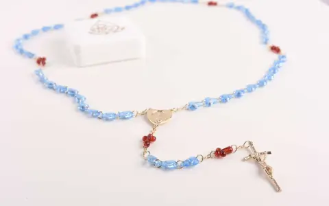 Niebieski różaniec z czerwonymi akcentami i krzyżem. Wybór różańca na roczek symbolizuje błogosławieństwo i duchową drogę.