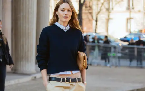 Modello con maglione blu scuro, camicia bianca e pantaloni beige. Un'idea su come vestirsi per uscire con stile.
