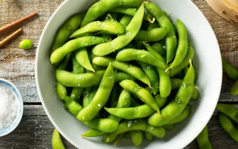 Salzige Edamame-Schoten in einer Schüssel, bereit zum Genießen. So isst man Edamame: die Schote aufbeißen und die Bohnen herausdrücken.