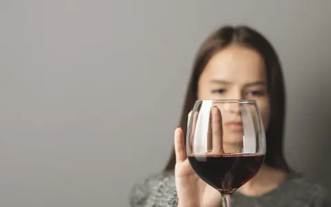 Kobieta odrzuca kieliszek z czerwonym winem, symbolizując walkę z pokusą, która może prowadzić do dawki śmiertelnej alkoholu.