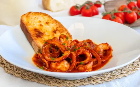 Moscardini in umido, teneri e saporiti, serviti con pane tostato e pomodorini freschi.