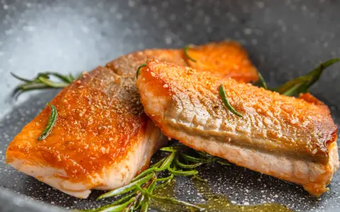 Zwei perfekt gebratene Lachsfilets mit knuspriger Haut und Rosmarin in einer Pfanne.