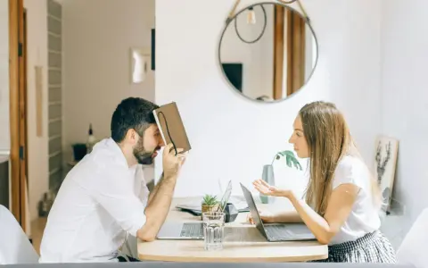 Hombre con personalidad narcisista, frustrado, se cubre la cara con un libro mientras una mujer le habla con exasperación.