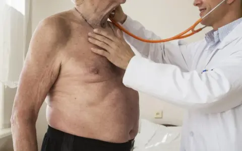 Lekarz osłuchuje klatkę piersiową starszego mężczyzny stetoskopem.
