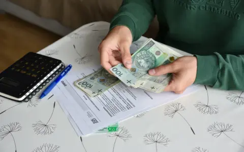Ręce liczą banknoty 100 zł nad dokumentami ZUS. Nowe zasady zasiłków przedemerytalnych w praktyce.