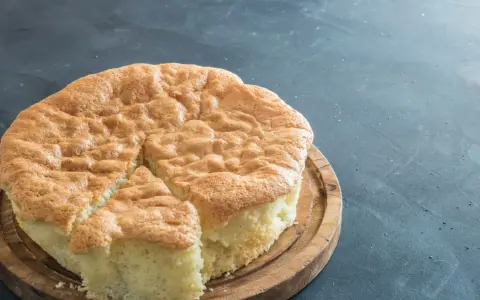 Un gâteau raté, un peu affaissé, sur une planche en bois. Sa texture est spongieuse et sa croûte dorée.