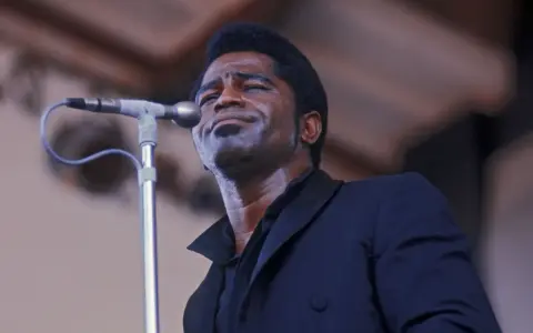 Le chanteur funk français James Brown, en sueur, chante passionnément dans un microphone.
