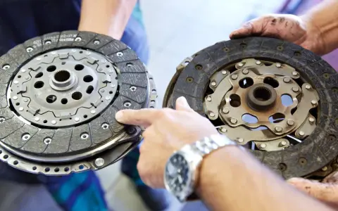 Mechanik pokazuje dwa dyski sprzęgła: jeden nowy, drugi mocno zużyty, z widocznymi śladami spalonego sprzęgła.