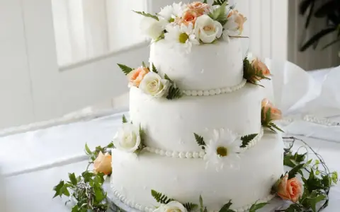 Elegancki tort weselny ozdobiony bukietem brzoskwiniowych i białych róż, margaretek i zieleni. Piękne, jakie żywe kwiaty na tort!
