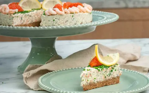 En läcker laxtårta på kavring, dekorerad med räkor, rom och citron. En bit serveras på en mintgrön tallrik.