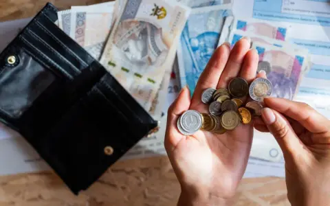 Otwarty portfel, polskie banknoty i monety w dłoni na tle dokumentów.