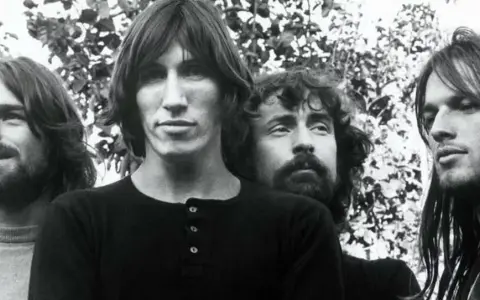 Quatre musiciens aux cheveux longs, dans un style musical Pink Floyd, posent devant un feuillage.