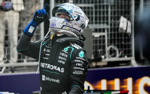 Piloto de F1 con casco y guantes azules levanta el dedo índice, celebrando una victoria en la carrera F1 Mónaco.