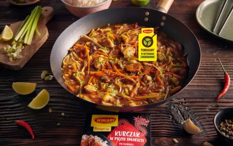 Kurczak w pięciu smakach po chińsku w woku, z warzywami i ryżem w tle. Obok limonki, chili i czosnek.