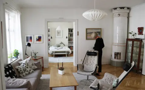 En kvinna i svart klänning står i ett rum med fransk inredningsstil. Ett sovrum syns i bakgrunden.