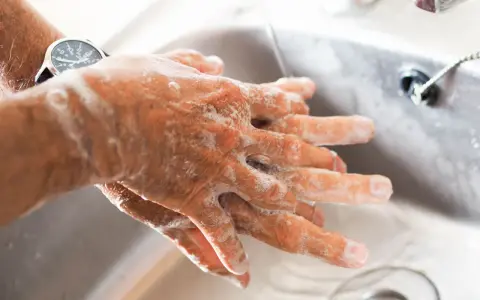 Manos con jabón bajo un chorro de agua en un lavabo.