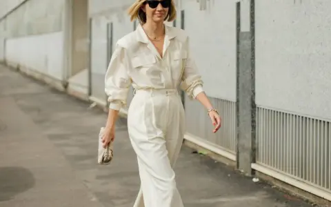 Mujer con un elegante outfit oficina verano: pantalón ancho blanco, camisa holgada y bolso de mano.