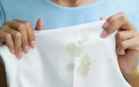 Manos sostienen tela blanca con manchas de grasa. Aprende como quitar la grasa de la ropa fácilmente.