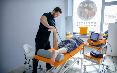 Fizjoterapeuta wykonuje zabieg naświetlania kręgosłupa pacjentowi leżącemu na kozetce.