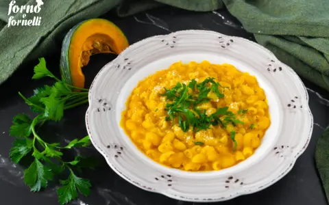 Piatto di pasta e zucca alla napoletana, guarnito con prezzemolo fresco e parmigiano. Accanto, una fetta di zucca e un mazzetto di prezzemolo.