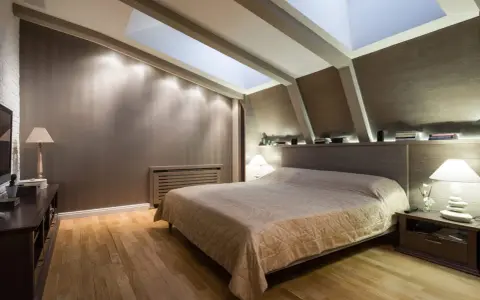 Chambre douillette avec un lit confortable sous une **tête de lit sous pente** et un puits de lumière illuminant la pièce.