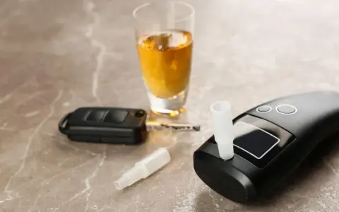 Alkomat, kluczyki samochodowe i kieliszek z alkoholem na marmurowym blacie.