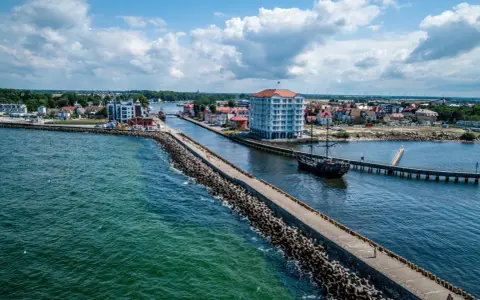 Widok na port w Darłówku Zachodnim z falochronem, budynkiem i statkiem pirackim.