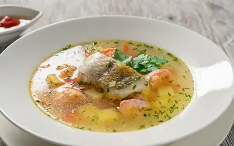 Aromatyczna zupa rybna przepis: delikatny filet rybny, kawałki łososia, ziemniaki i marchewka w bulionie, ozdobiona natką pietruszki.