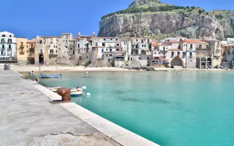 Coastal town with buildings nestled against a cliff, turquoise water, and boats. Perfect for a 10 days in Sicily adventure.
