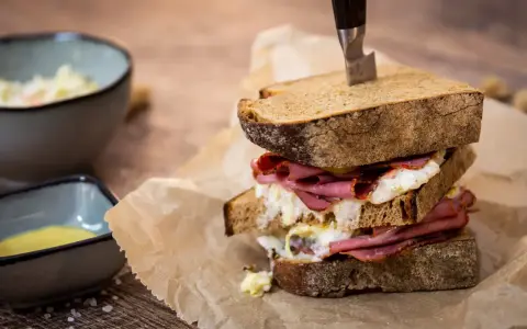 Ein üppiges Pastrami-Sandwich mit Röstbrot, serviert mit Beilagen wie Krautsalat und Senf.