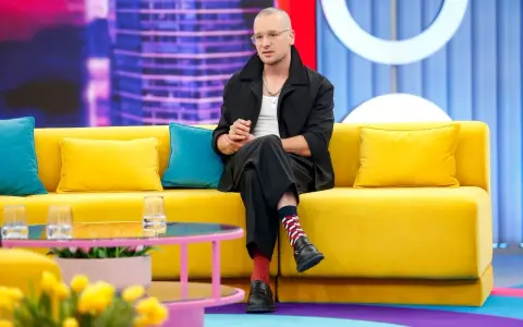 Krzysztof Zalewski w czarnym garniturze siedzi na żółtej kanapie, jakby przygotowywał się do nagrania jednego z jego filmów.