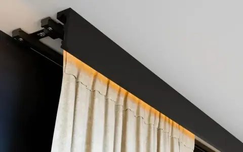 Nowoczesna szyna sufitowa z ukrytym oświetleniem LED, na której wiszą beżowe zasłony. Eleganckie rozwiązanie zamiast tradycyjnego karnisza.