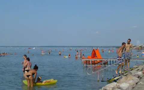 Tłum ludzi cieszy się słońcem i wodą. Dzieci bawią się na dmuchanej zjeżdżalni, a dorośli pływają i relaksują się. Wszyscy zasila Balaton w gorący letni dzień.