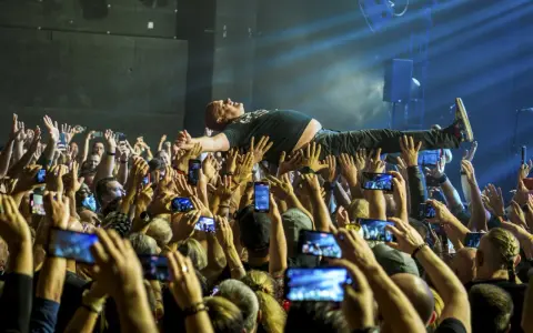 Kult w Arahji: wokalista zespołu niesiony przez tłum, fani nagrywają koncert telefonami.