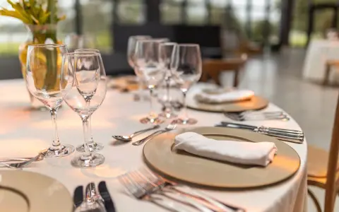 Une table élégamment dressée pour un repas, avec la position des verres à la française. Des assiettes, serviettes et couverts sont prêts.