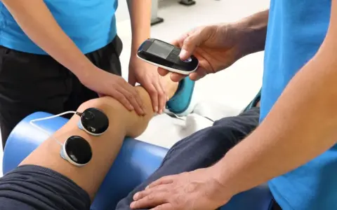 Rehabilitacja: fizjoterapeuta z urządzeniem do elektroterapii przy nodze pacjenta.