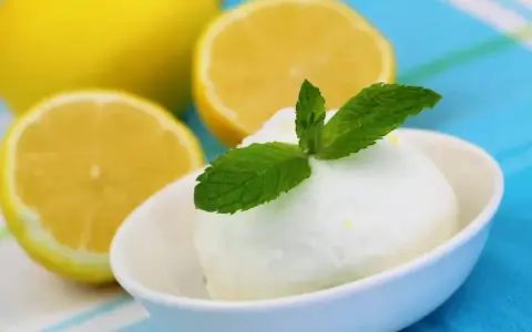 Crème glacée citron rafraîchissante, garnie de menthe fraîche, avec des citrons coupés en arrière-plan.