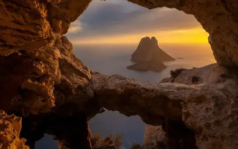 Widok z jaskini na skalistą wysepkę Es Vedrà, jedną z najpiękniejszych wysp Balearów, o zachodzie słońca.