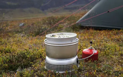 Matlagning på ett esbit kök i fjällen. En kastrull med mat värms upp bredvid ett tält.