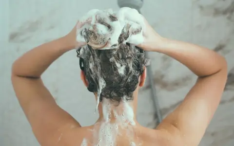 Person wäscht sich die Haare mit schaumbildendem Shampoo. Die Stiftung Warentest hat Olaplex-Produkte untersucht.