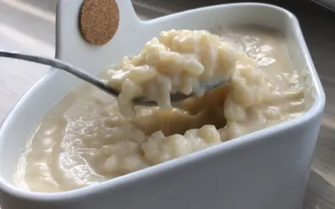 Cuillère prélevant une portion crémeuse de riz au lait dans un bol blanc.