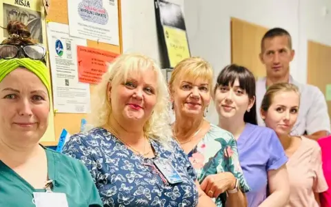 Grupa uśmiechniętych pracowników medycznych w szpitalu, na tle tablicy ogłoszeń.