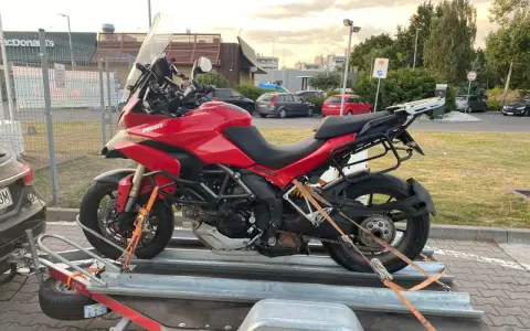 Czerwony Ducati na przyczepie, zabezpieczony pasami do transportu. Gotowy do drogi.